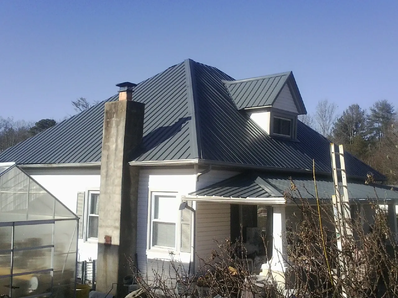 Dark blue standing seam metal roof on a white farmhouse with dormer — Slate & Tile Roof Repair by Roofing Brothers in Wilsons Mills