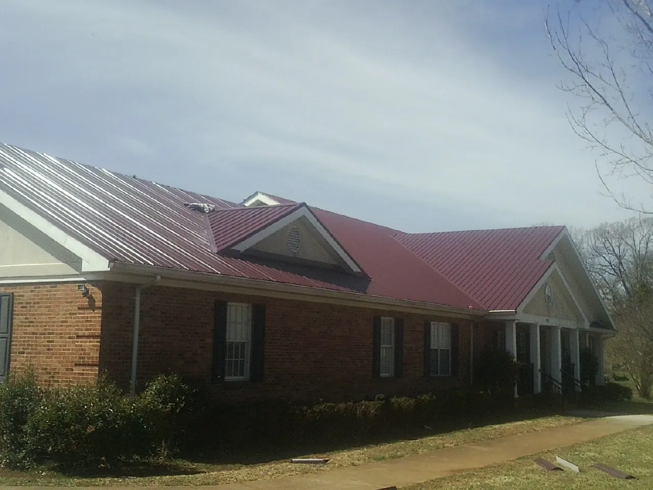Red metal roof with gabled entries on a long brick building, from a Hail Damage Roof Repair job in Wilsons Mills