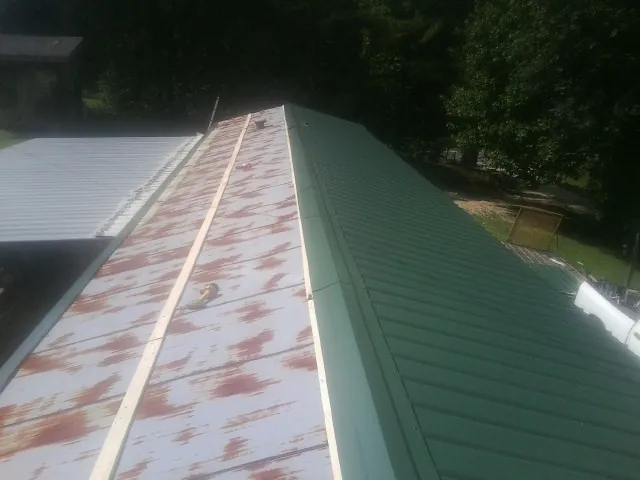 Old rusted panels beside newly installed green metal roofing — Wind Damage Roof Repair by Roofing Brothers in Wilsons Mills