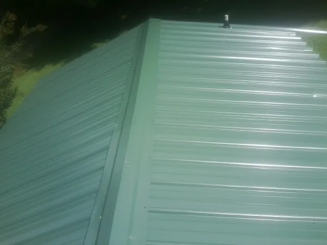 New green metal panels meeting at the ridge of a roof — Flat Roof Repair work by our crew in Wilsons Mills