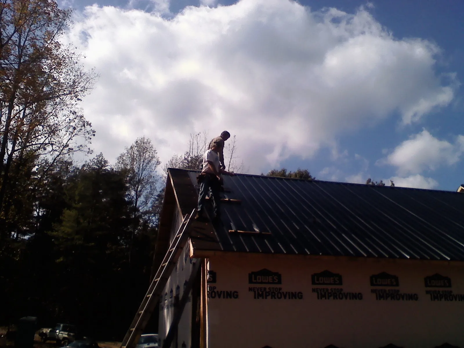 Roofer fastening dark metal panels high against a cloudy sky, from a Roof Inspection job in Wilsons Mills