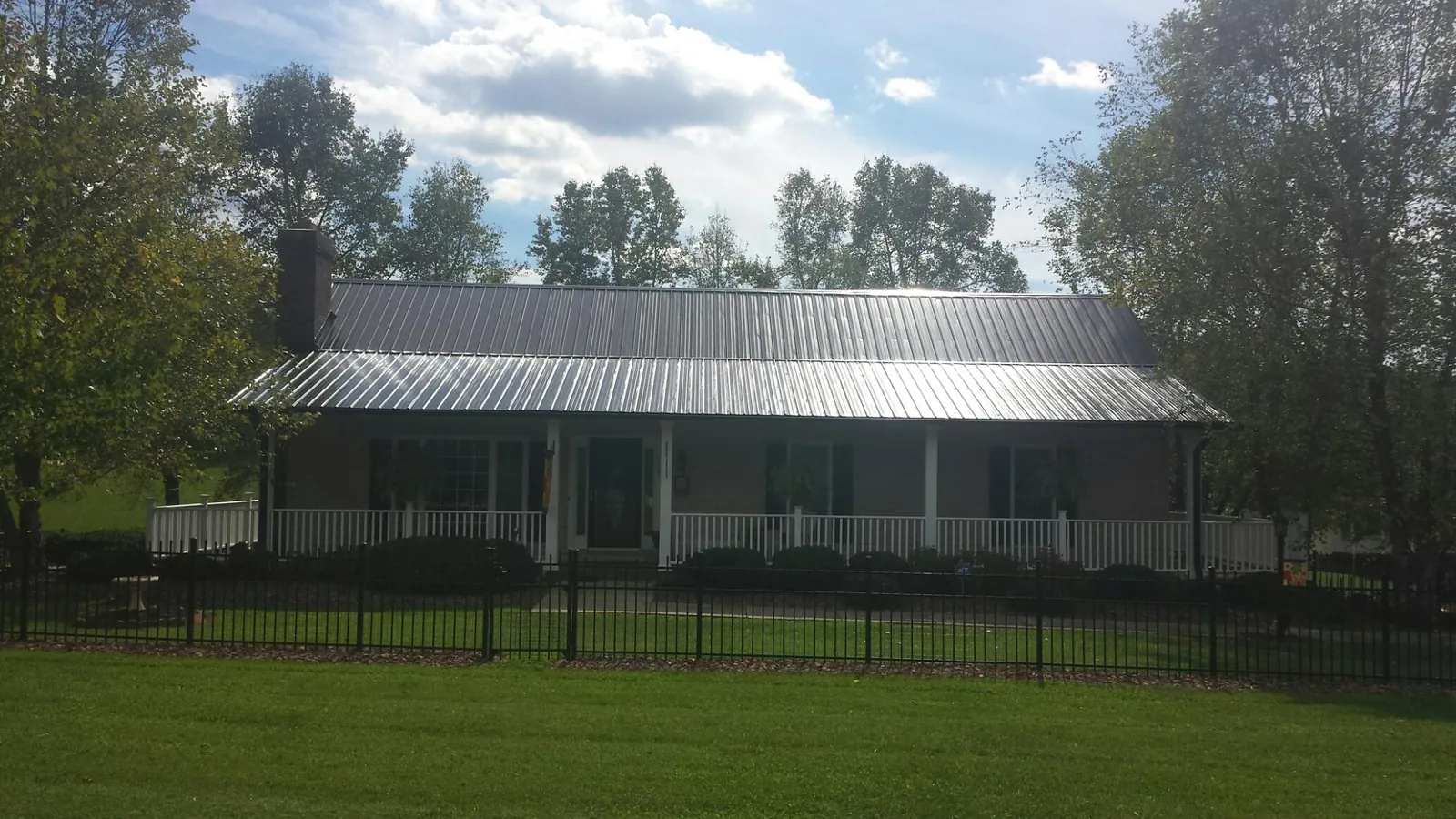 Gray metal roof on a brick ranch with a full width front porch — Gutter Guard Installation work by our crew in Wilsons Mills