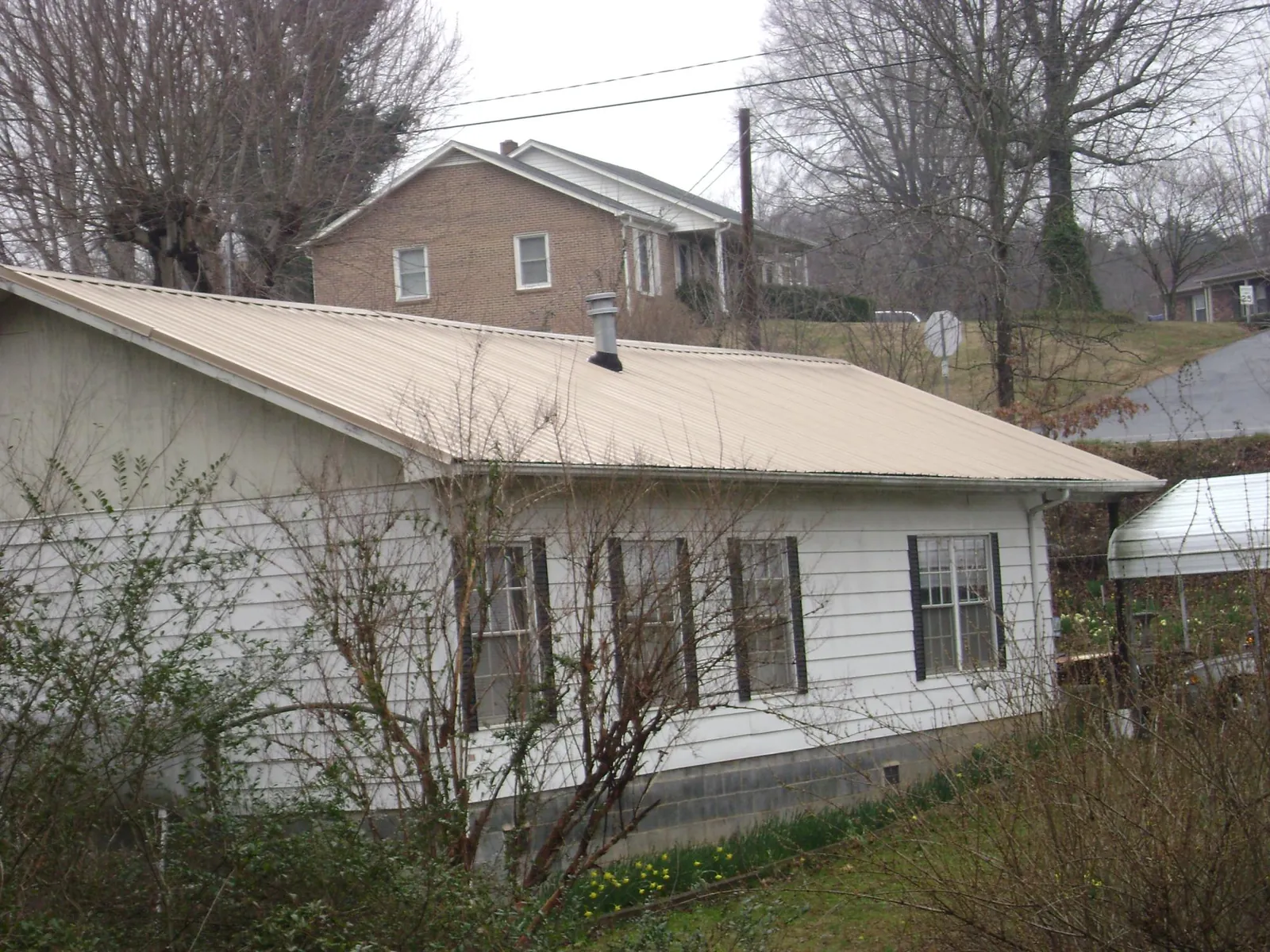 Tan metal roof on a white sided house set into a hillside — Commercial Roofing by Roofing Brothers in Wilsons Mills