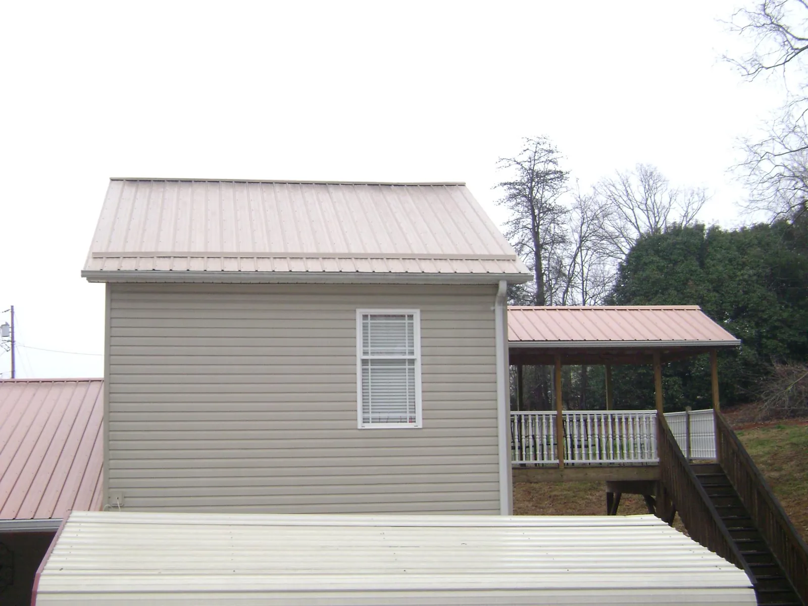 Tan metal roofs on a two story addition and attached porch, from a Roof Replacement job in Wilsons Mills